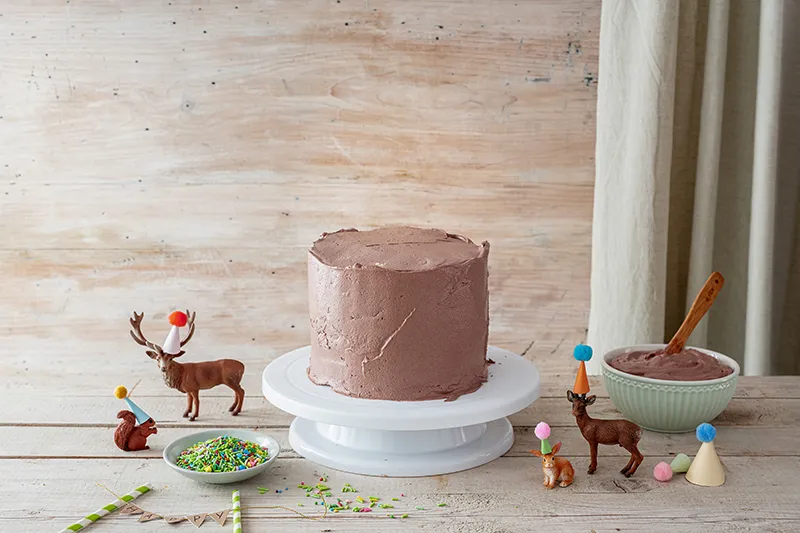 Glatt gestrichener Geburtstagskuchen mit cremiger Schokoladencreme als Basis für die Waldtiere-Dekoration