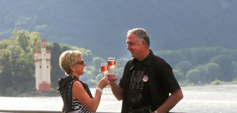 Glückliches Paar stößt mit Wein am malerischen Rheinufer an, perfekt für einen entspannten Urlaub am Rhein
