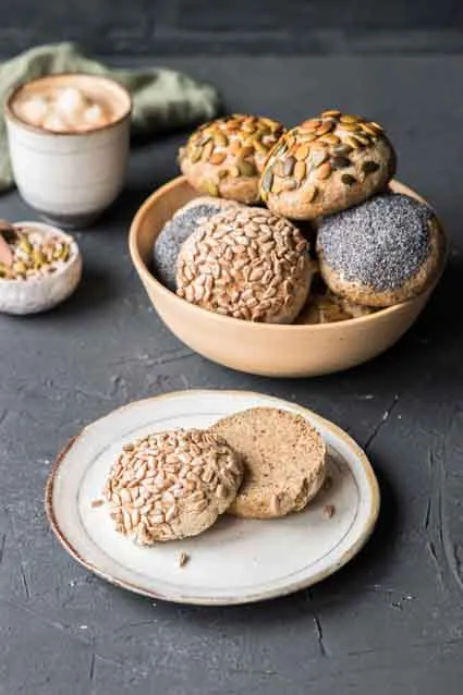 Glutenfreie Reismehl-Frühstücksbrötchen mit Kürbis- und Sonnenblumenkernen auf Backpapier, frisch aus dem Ofen.