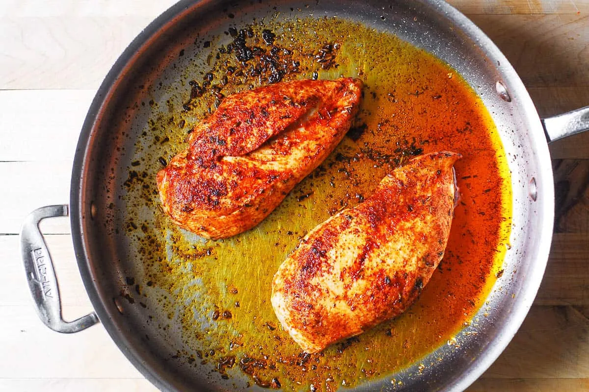 Goldbraun gebratene Hähnchenbrustfilets in einer Edelstahlpfanne, gewürzt mit Paprika und italienischen Kräutern.