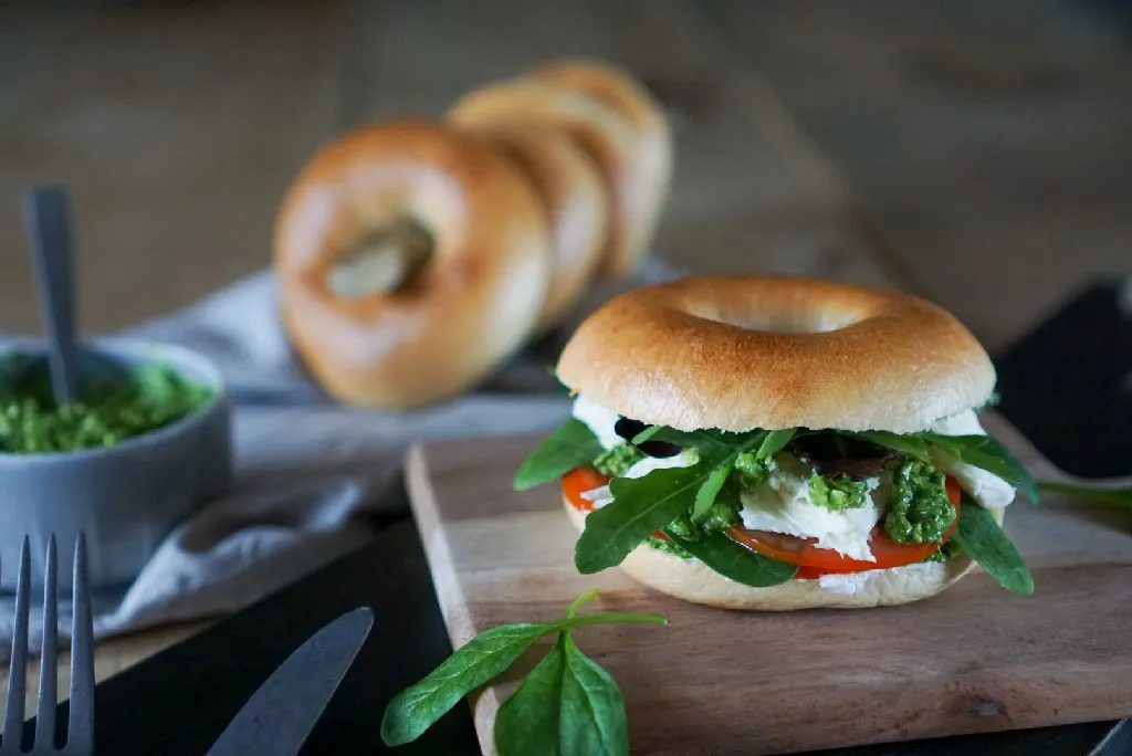 Goldbrauner Bagel belegt mit Tomaten, Mozzarella und frischem Spinatpesto