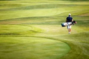 Golfer geht mit Schläger und Tasche über einen sonnigen Golfplatz.