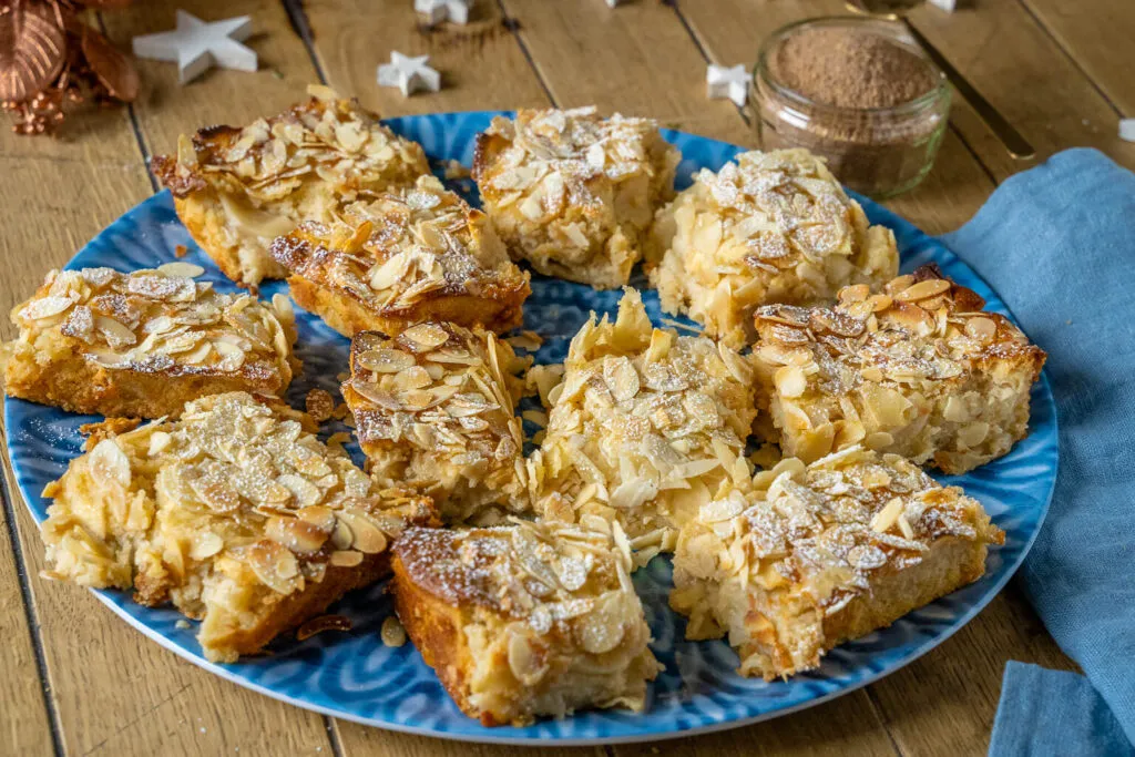 Großes Stück Apfelkuchen mit Marzipan auf einem Teller, bereit zum Servieren, mit Fokus auf die saftige Apfelfüllung und Marzipannote