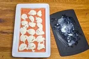 Hackbällchen in der Auflaufform, bedeckt mit Tomatensoße und belegt mit Mozzarella-Scheiben vor dem Backen