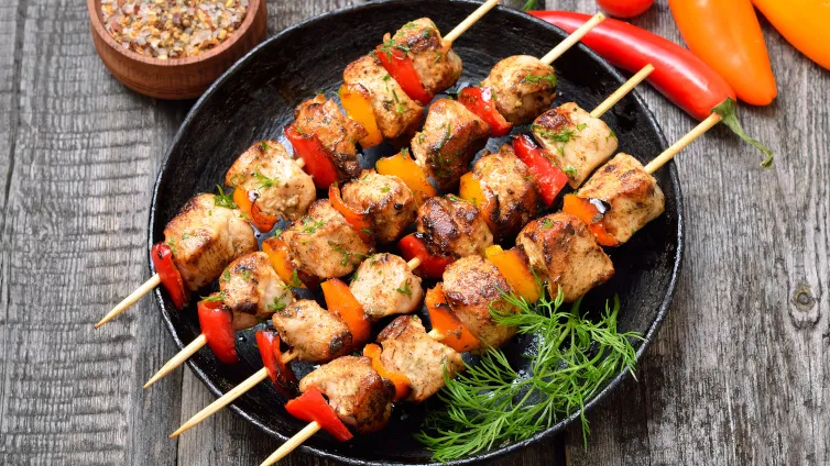 Hähnchenspieße mit frischer Paprika und einem würzigen Dressing, appetitlich angerichtet auf einem dunklen Teller.