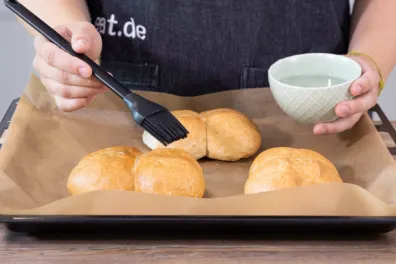 Hand befeuchtet trockene Brötchen mit Wasser vor dem Aufbacken im Ofen