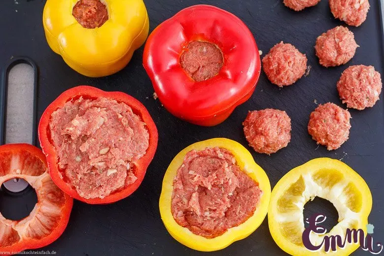 Hand füllt eine rote Gemüsepaprika sorgfältig mit einer rohen, gut gewürzten Hackfleischmasse, symbolisierend den Beginn der Zubereitung eines deutschen Hausmannskost-Klassikers.