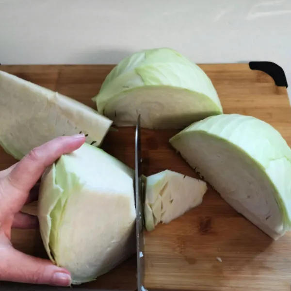 Hand schneidet einen Kopf grünen Kohls auf einem Holzschneidebrett in große Keile.