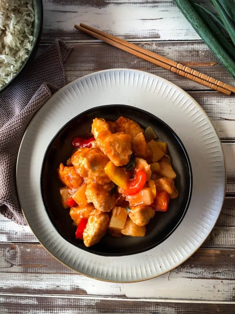Hausgemachtes Hähnchen süß-sauer mit Reis, angerichtet auf einem Teller, perfekt wie aus dem China-Restaurant.