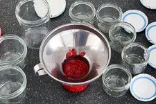 Heiße, frische Himbeermarmelade wird in sterile Schraubgläser gefüllt, um die Haltbarkeit zu gewährleisten.