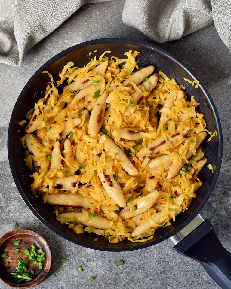 Herzhaft angebratenes Sauerkraut mit veganen Schupfnudeln in einer schwarzen Pfanne, ein beliebtes deutsches Gericht.