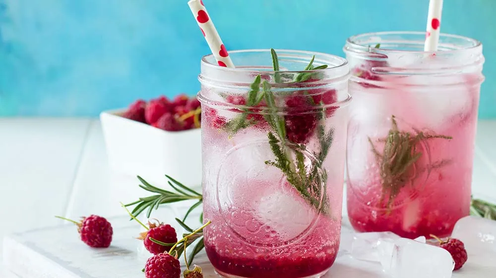 Himbeer Punch alkoholfrei, garniert mit frischen Himbeeren und Rosmarin, serviert in einem Glas mit Eiswürfeln