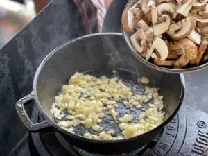 Hinzufügen von geschnittenen Champignons zu den angedünsteten Zwiebeln für die Stroganoff-Sauce