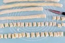 In Stücke geschnittener Gnocchi-Teig auf einer Arbeitsfläche, die typische Nockenform entsteht.
