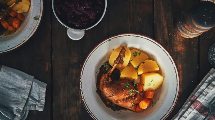 Kaninchenbraten mit knuspriger Haut, serviert mit Salzkartoffeln, Rotkohl und frischen Kräutern in einem rustikalen Topf.