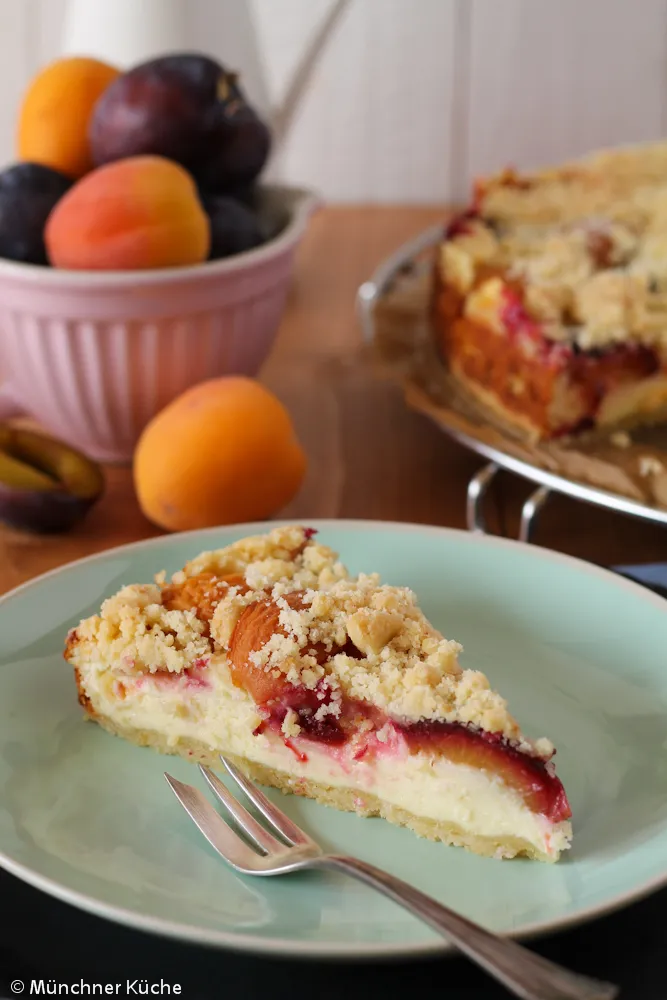 Käsekuchen mit frischen Aprikosen, Zwetschgen und knusprigen Streuseln, bereit zum Genießen.
