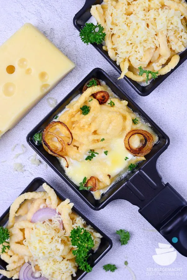 Käsespätzle im Raclette Pfännchen, goldbraun überbacken mit gerösteten Zwiebeln, eine deftige und beliebte vegetarische Raclette Variante.