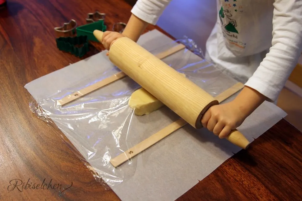 Kind rollt Keksteig mit Frischhaltefolie aus