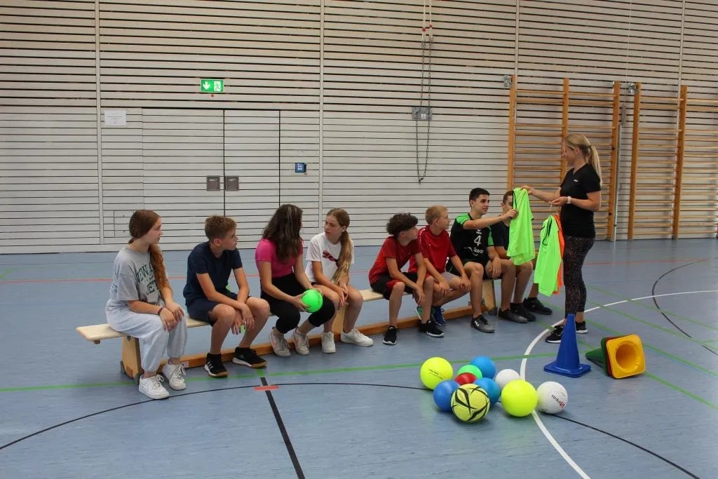 Kinder und Jugendliche in einer Turnhalle, aufgeteilt für dynamische Aufwärmübungen im Sportunterricht