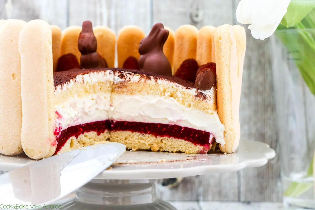 Klassische sahnetorte zu Ostern mit frischen Himbeeren und Schoko-Osterdekoration, umrandet von Löffelbiskuit.