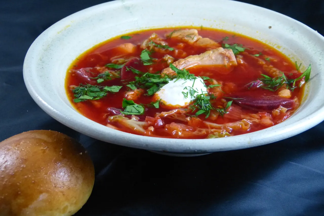 Klassischer roter Borschtsch mit frischer Sahne und Dill, serviert mit duftenden Knoblauchbrötchen Pampuschki.
