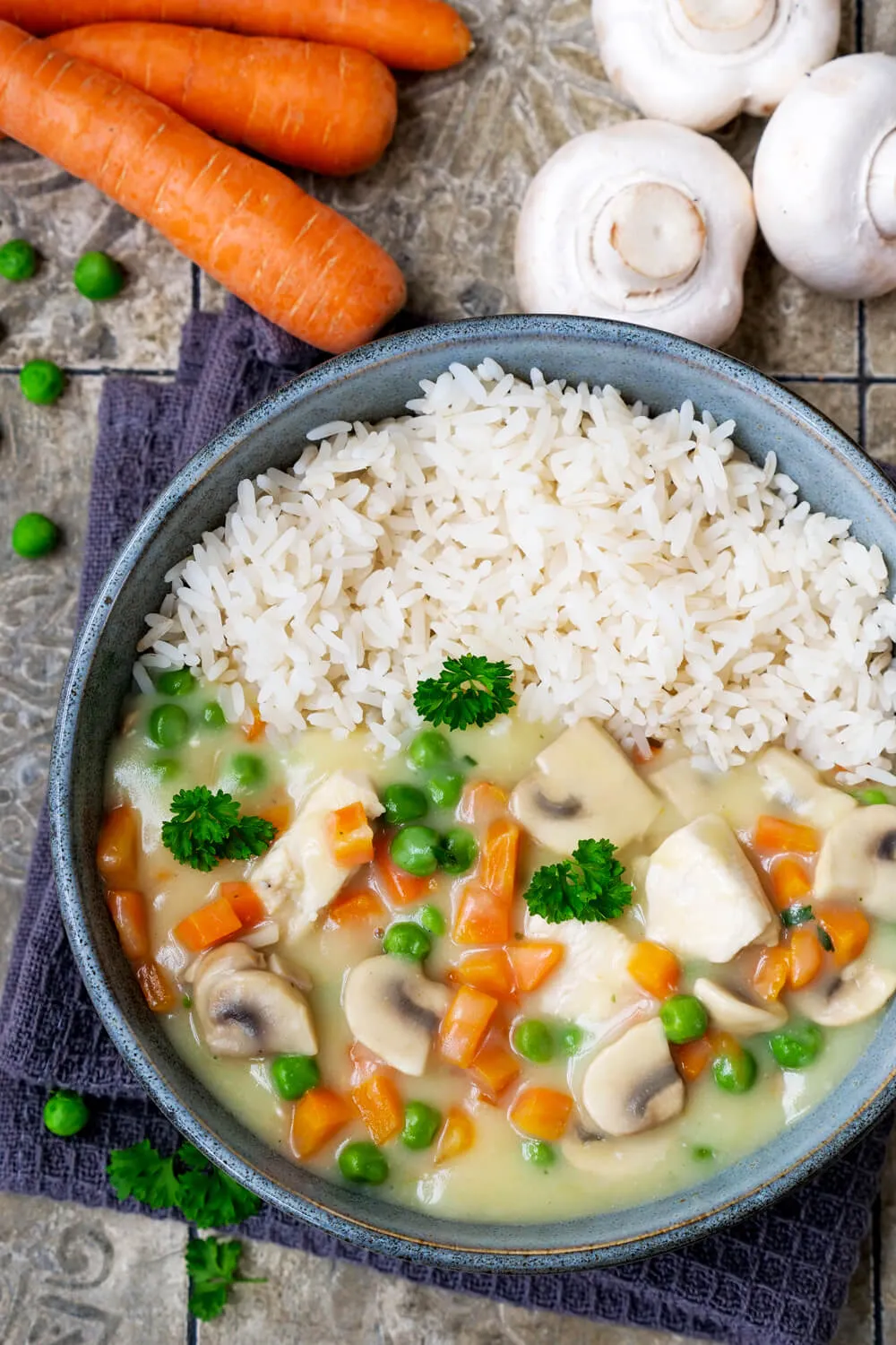 Klassisches Hühnerfrikassee mit Hähnchen, Gemüse und Reis. Alternative Text: Klassisches Hühnerfrikassee mit Hähnchenfleisch, Erbsen, Möhren und Reis in einer weißen Schüssel, perfekt für ein gesundes Mittagessen.