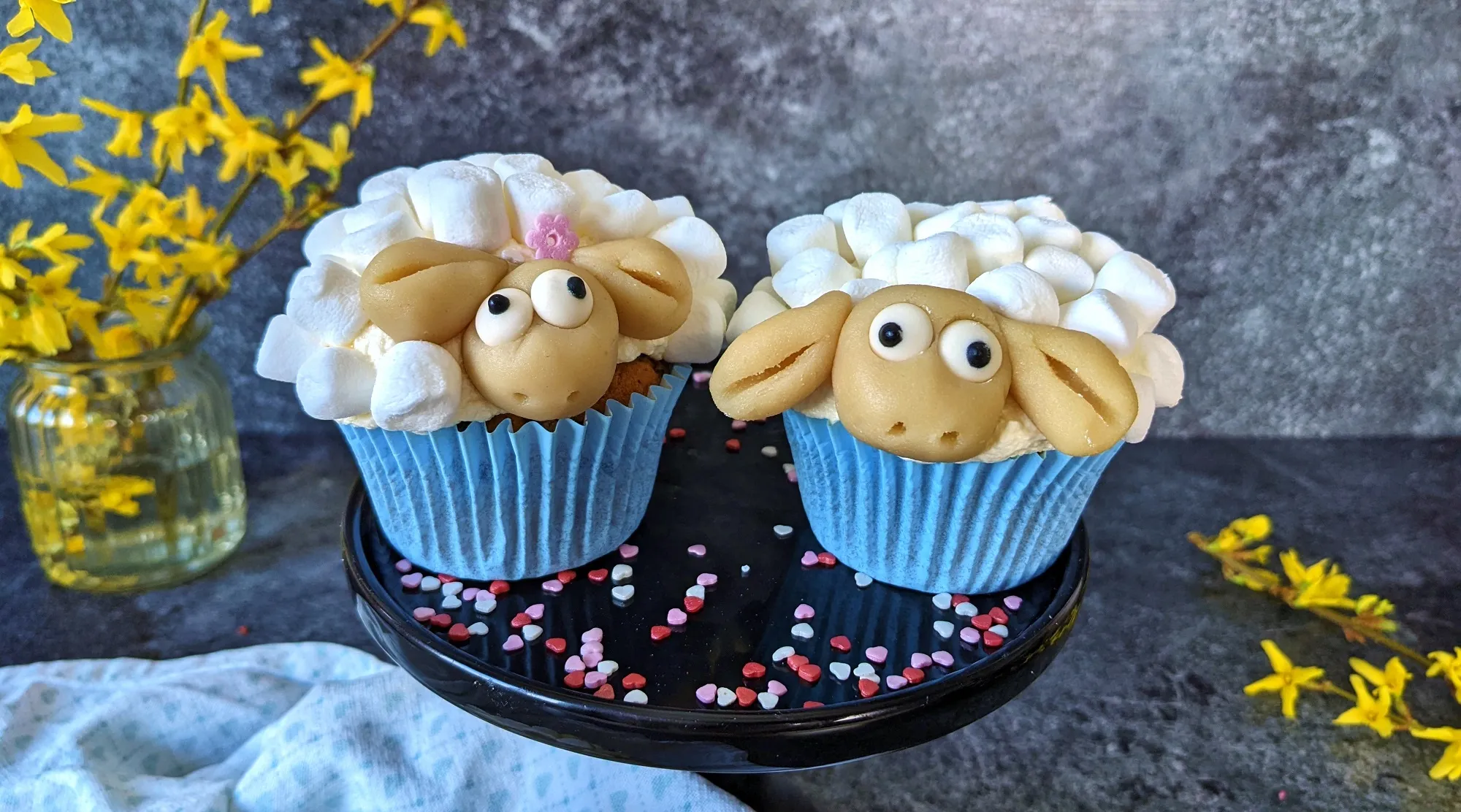 Kleine Herde fertiger Schaf-Muffins mit blumiger Dekoration auf einer grünen Unterlage