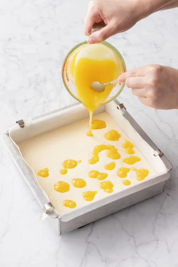 Kleine Kleckse leuchtend gelbes Lemon Curd werden auf Käsekuchenteig gegeben.