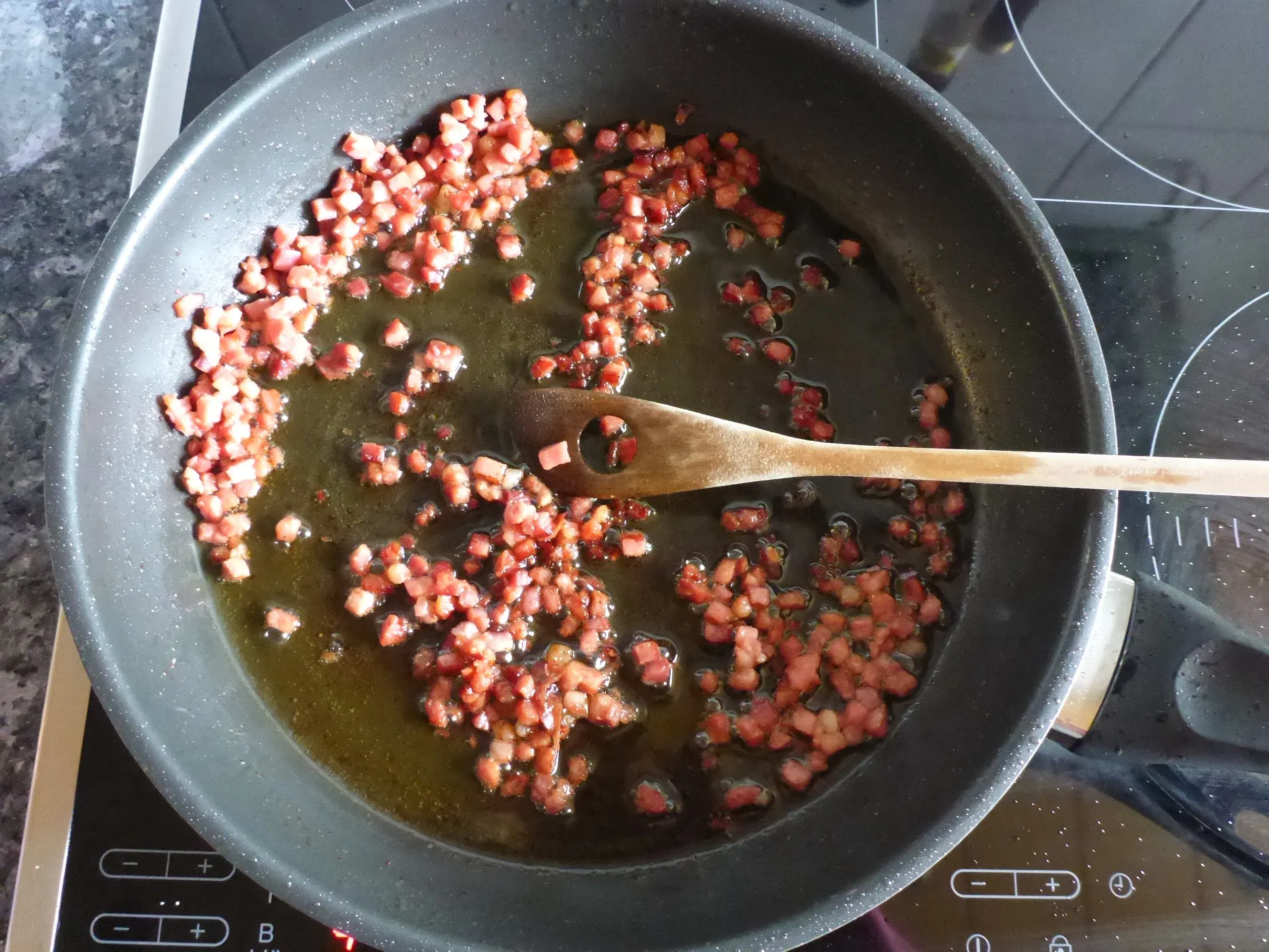 Knusprig gebratene Speckwürfel in einer Pfanne, die später der Lauch-Pilz-Rahmsauce der Schnitzelpfanne eine würzige Note verleihen.
