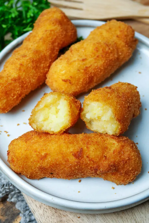 Knusprige Kartoffel-Kroketten appetitlich auf einem weißen Teller angerichtet.