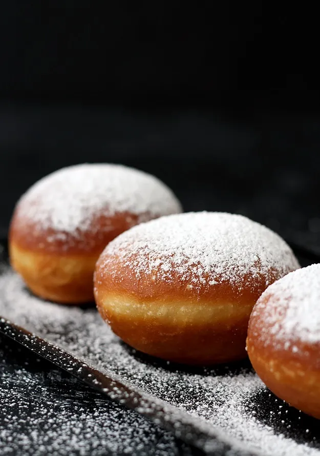 Krapfen nach dem Frittieren mit Puderzucker bestreuen