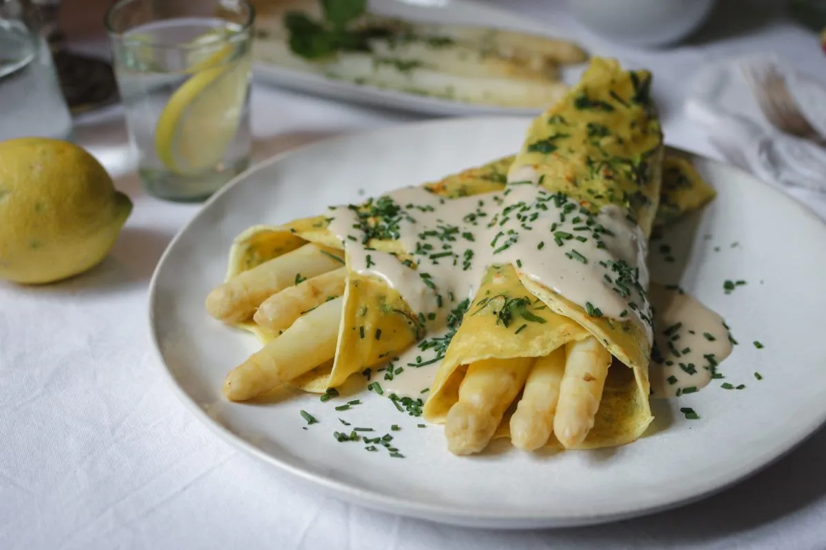 Kreatives Spargelrezept: Weißer Spargel in einem veganen Kräuterpfannkuchen, kunstvoll angerichtet.