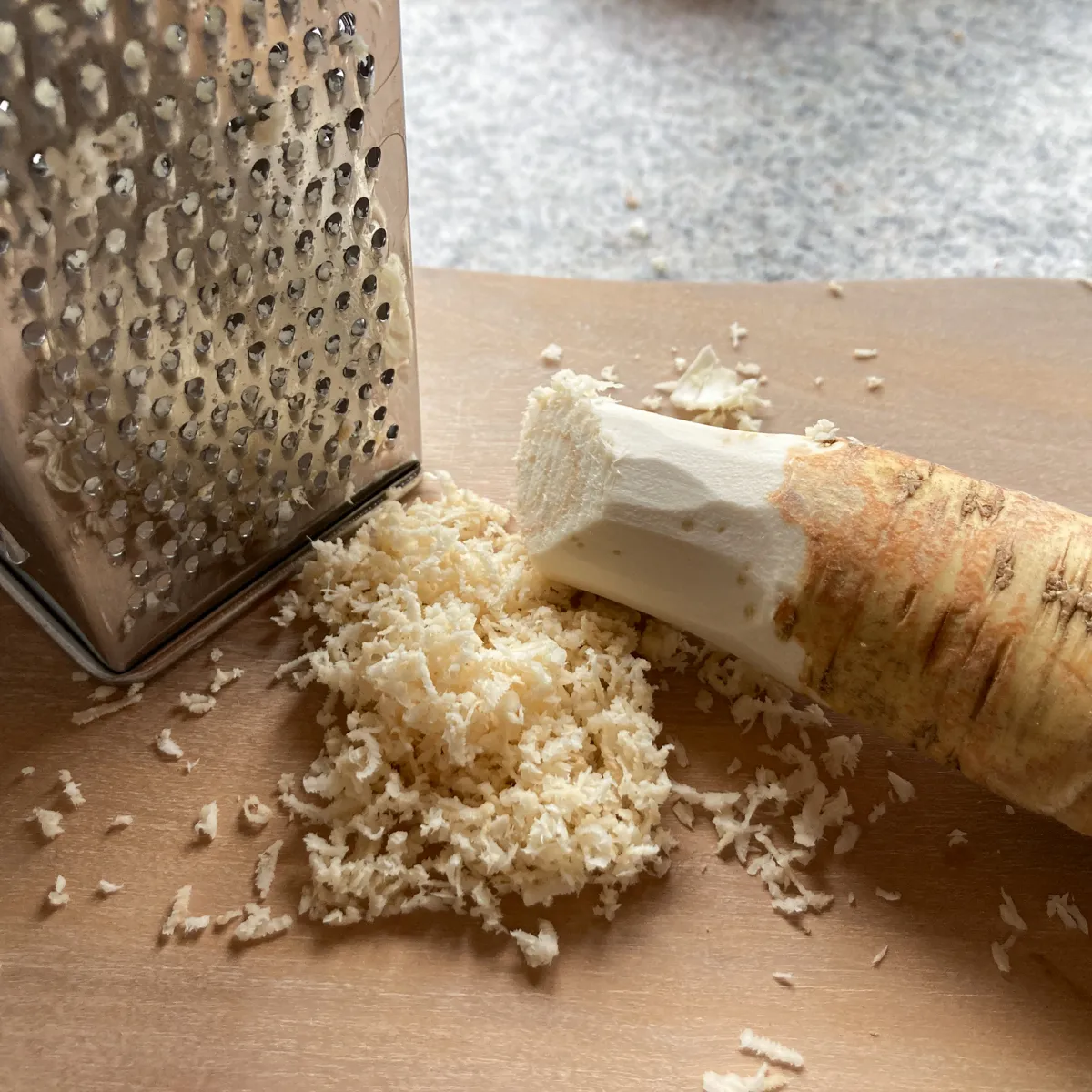 Kren abgerieben mit Vierkantreibe auf Holzbrett. Frisch geriebener Kren verströmt sein intensives Aroma und verleiht der Semmelkren die typische Schärfe.