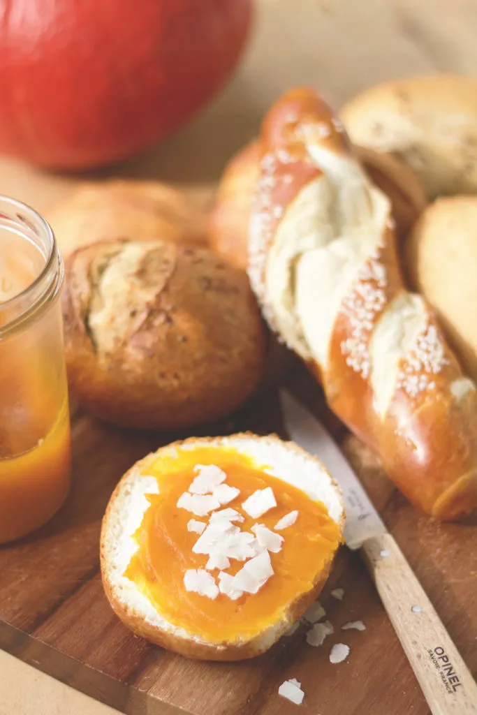 Kürbis-Kokos-Konfitüre in einem Glas auf einem Holztisch, im Hintergrund frische Früchte