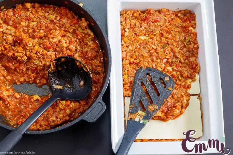 Lasagneplatten und Gemüsesoße werden in einer Auflaufform geschichtet, bereit für den Ofen