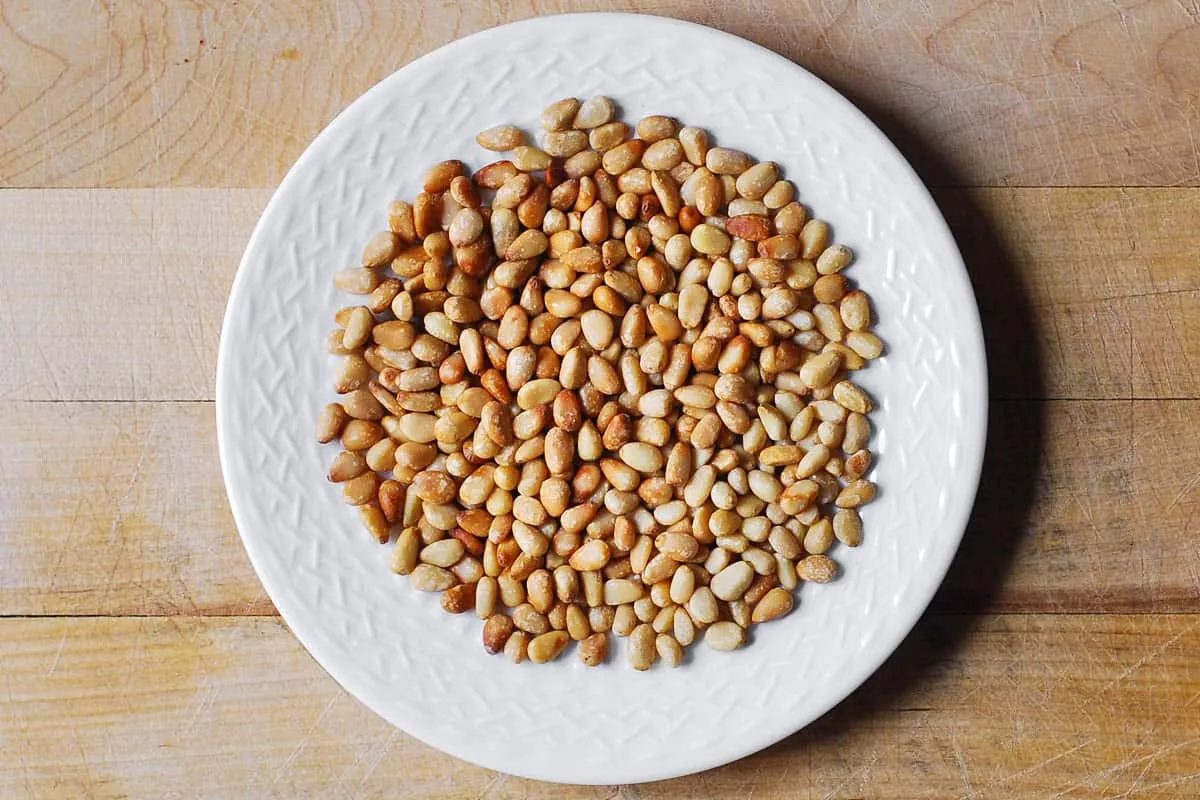 Leicht geröstete Pinienkerne auf einem weißen Teller, bereit, der Hähnchen Pasta ihren knusprigen Biss zu verleihen.