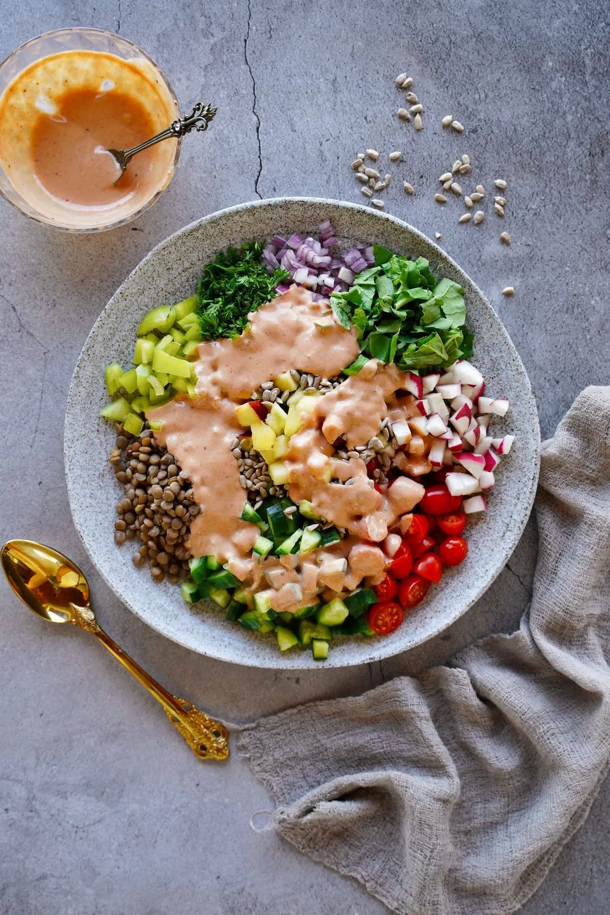 Linsensalat mit frischen Kräutern, Äpfeln und cremiger Tahini-Dressing auf einem grauen Teller, ein schnelles veganes Mittagessen.