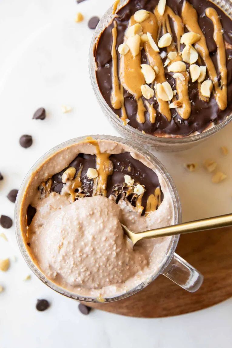 Löffel nimmt cremige Snickers Overnight Oats aus einem Glas mit Schokoladenüberzug.