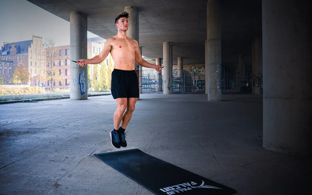 Mann springt Seil auf einer gelenkschonenden Trainingsmatte unter einer Brücke.