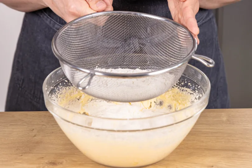 Mehl und Backpulver in den Kuchenteig sieben