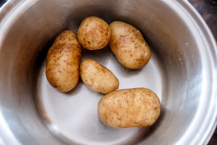 Mehlig kochende Kartoffeln mit Schale im Kochtopf für die Schupfnudel-Zubereitung.