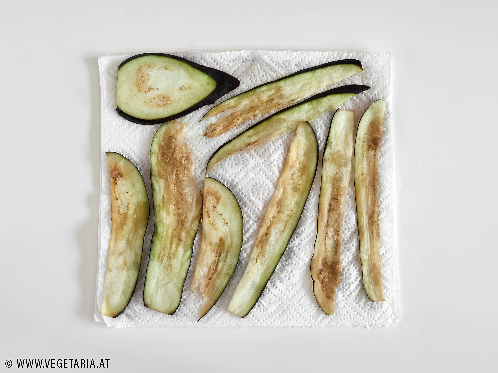 Melanzanischeiben werden zwischen Lagen von Küchenpapier gelegt, um überschüssiges Wasser zu entfernen.