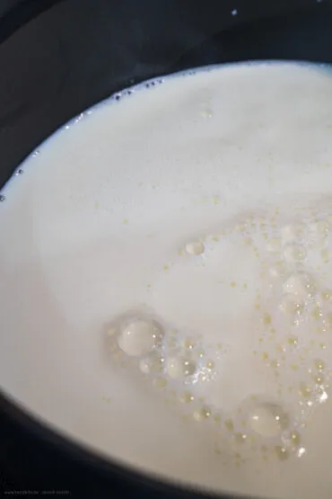 Milch wird in einem Topf auf dem Herd erhitzt für die Frischkäseherstellung.