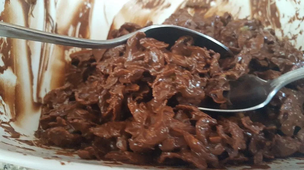 Mit zwei Löffeln werden kleine Häufchen der Schoko-Cornflakes-Mischung geformt.