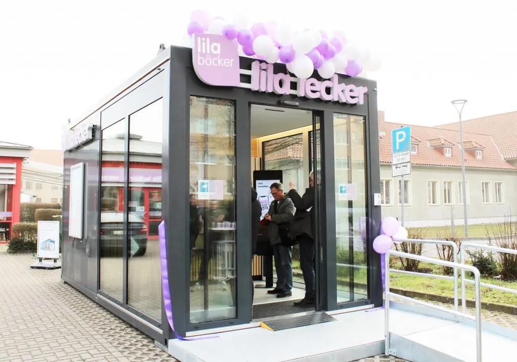 Moderner Lila Bäcker Pick-up-Store von außen, bodentief verglast, bereit für flexible Standortwechsel und 24/7-Verkauf frischer Backwaren in Neubrandenburg.