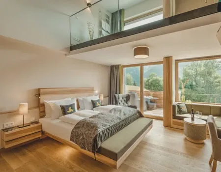 Modernes Hotelzimmer mit Doppelbett, gemütlicher Sitzecke und großen Fenstern mit Blick ins Grüne im Wellnesshotel Klosterhof in Bayern.