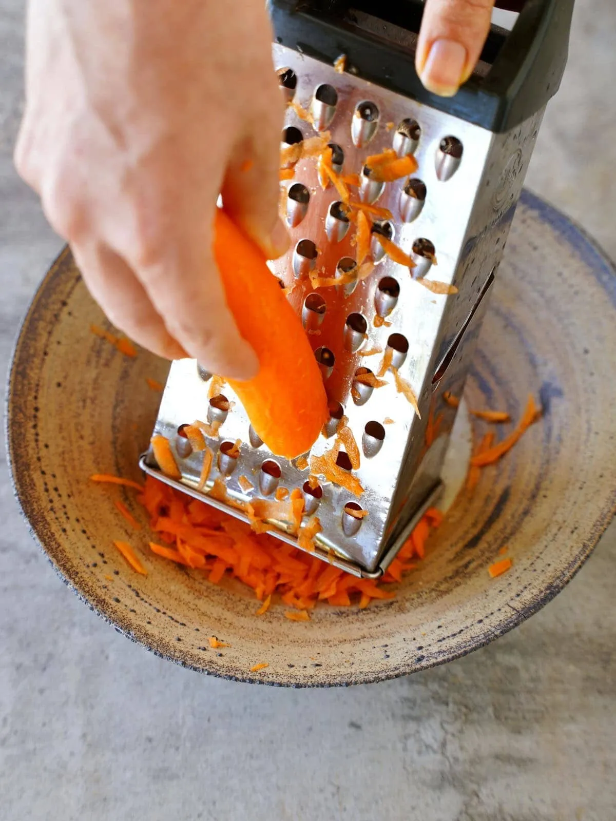 Möhren werden mit einer Reibe geraspelt