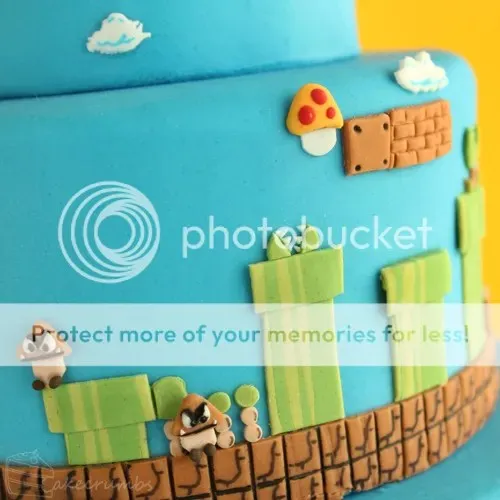 Nahaufnahme der zweiten Ebene des Super Mario Geburtstagskuchens mit detailreichen grünen Rohren, braunen Blöcken und Wolken aus Fondant.