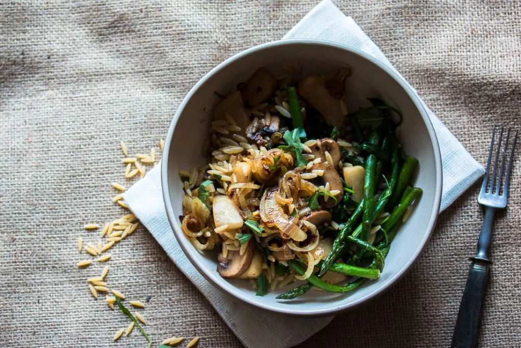Nahaufnahme des fertig angerichteten Orzo-Gerichts mit Mairübchen, braunen Champignons und grünem Spargel, bestreut mit Zwiebeln