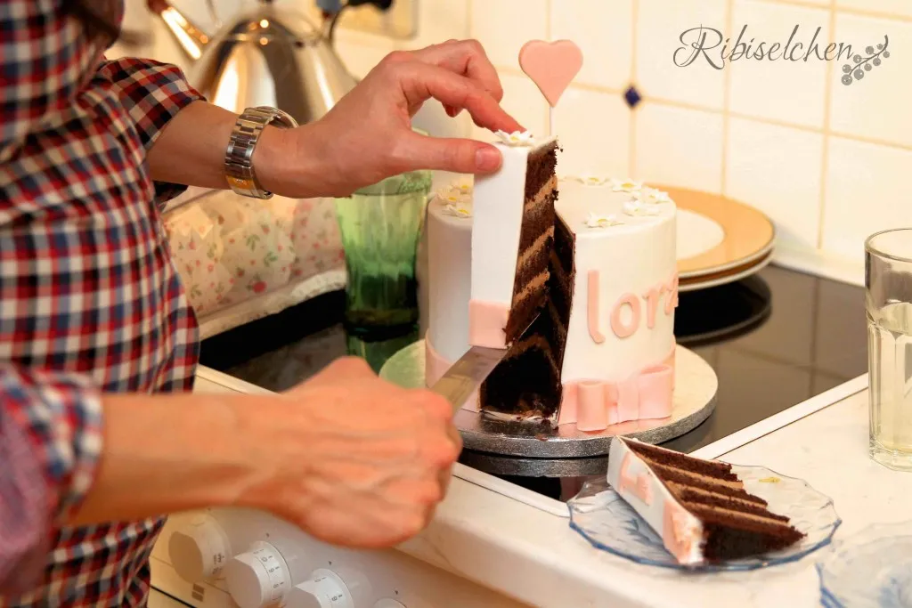 Nahaufnahme des Namens &quot;Flora&quot;, detailreich aus Modellierschokolade gefertigt und auf einer zarten Rosentorte platziert